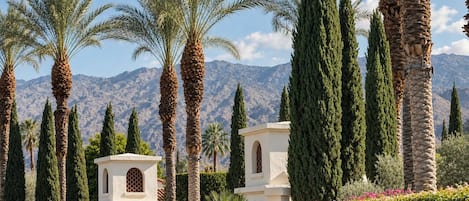 Un complexe hôtelier bordé de palmiers et de cyprès, avec une chaîne de montagnes en toile de fond.