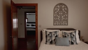 A bedroom with a bed, pillows, a decorative wall piece, and a wooden door.
