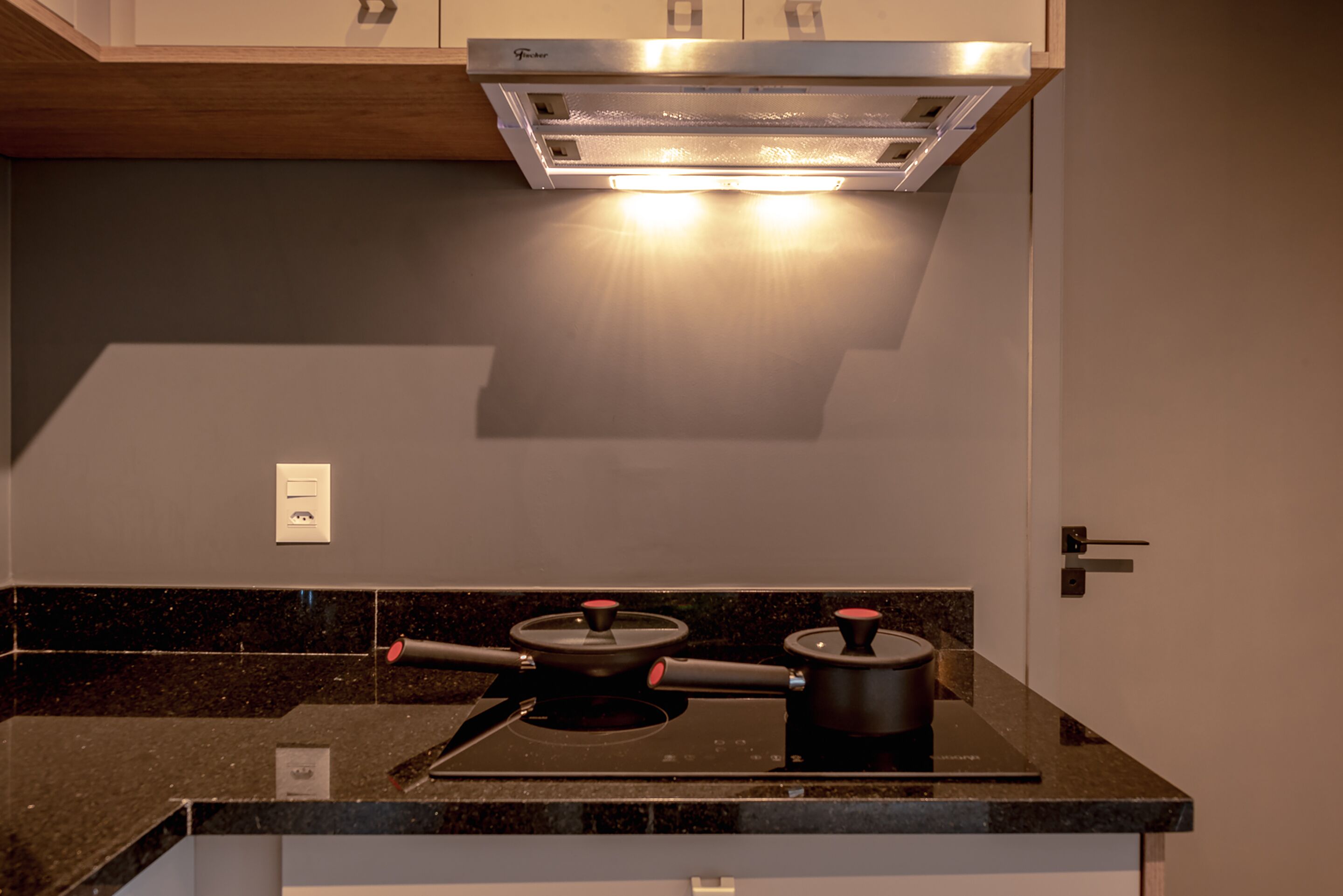 A kitchen with a modern design, featuring a black countertop, stainless steel range hood, and a built-in stove.