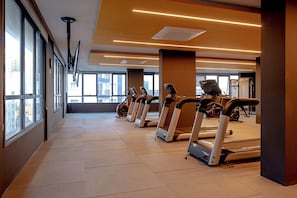 Ein Fitnessstudio mit in Reihen angeordneten Laufbändern, großen Fenstern und einem modernen Innenraum.