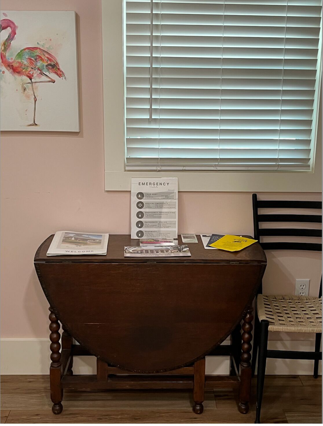 A wooden table with a welcome sign, emergency instructions, and a framed artwork on the wall.