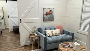 Een gezellige woonkamer met een blauwe bank, een klein houten bijzettafeltje, een ronde houten salontafel en een kamerkleed met een patroon.