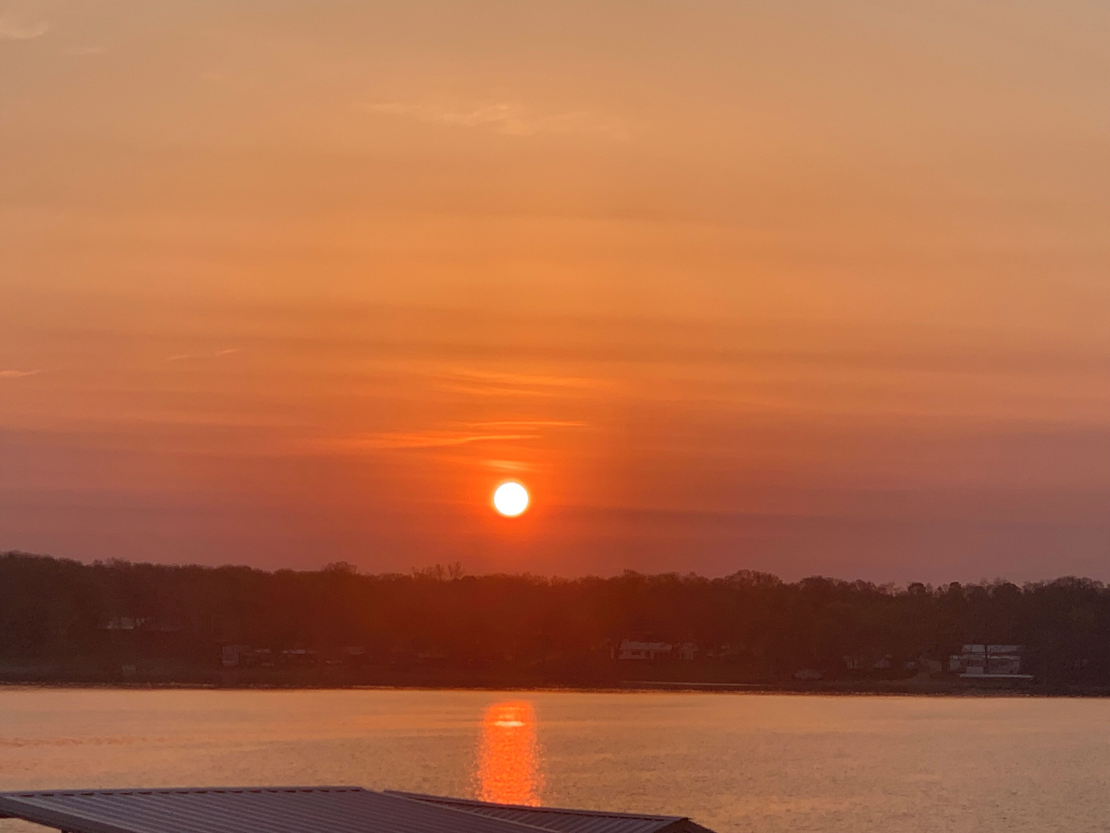 A sunset over a calm body of water with a dock in the foreground.