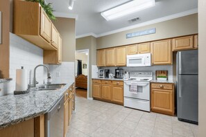 A modern kitchen with wooden cabinets, a granite countertop, stainless steel appliances, and a sign that reads "be our guest."