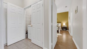 Un couloir avec des portes blanches menant à une chambre à coucher qui contient un lit et une table de chevet.