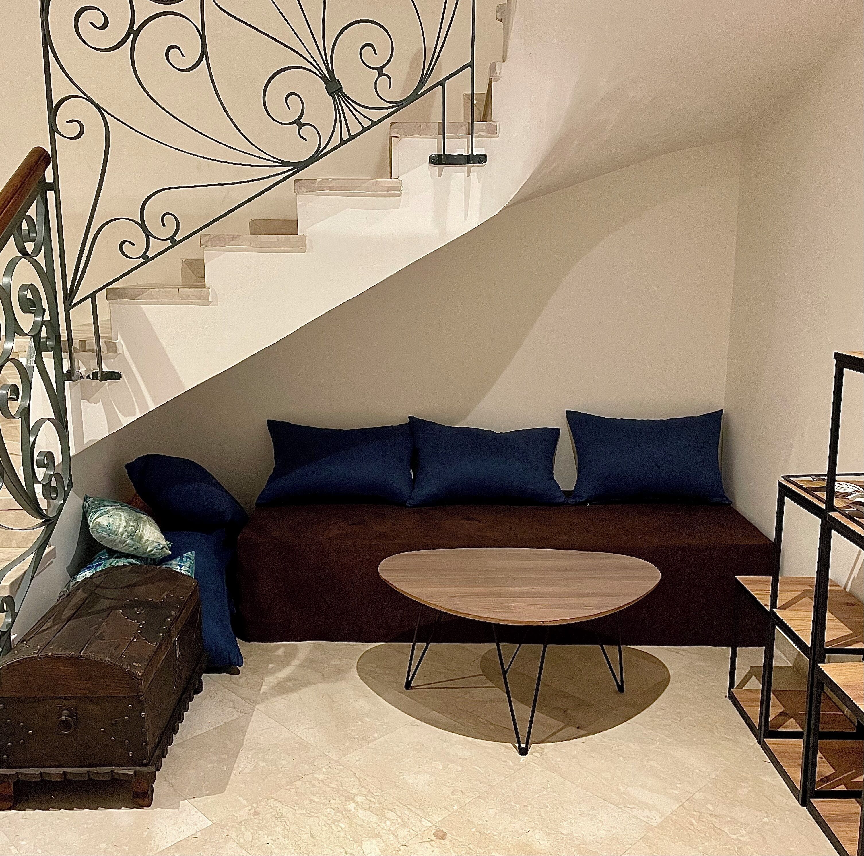 A modern living room with a brown sofa, two blue cushions, a round wooden coffee table, a metal spiral staircase, and a vintage suitcase.