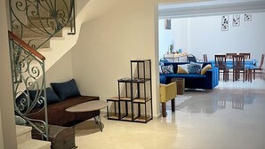 A spacious living area with a blue sofa, a small table, and a staircase with decorative metal railings. - Modern 140 m² duplex - 2 bedrooms with terrace and shared swimming pool. Gueliz. (Marrakech)
