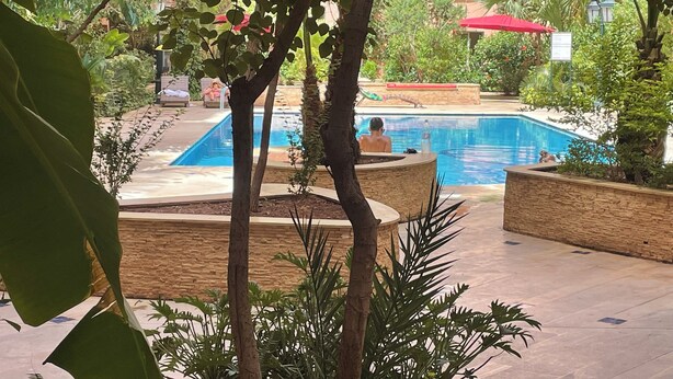 A pool area with a clear view of the water, surrounded by plants and a stone wall. - Modern 140 m² duplex - 2 bedrooms with terrace and shared swimming pool. Gueliz. (Marrakech)