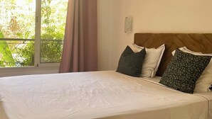 A neatly made bed with a wooden headboard, a large window with curtains, and a woven wall hanging. - Modern 140 m² duplex - 2 bedrooms with terrace and shared swimming pool. Gueliz. (Marrakech)