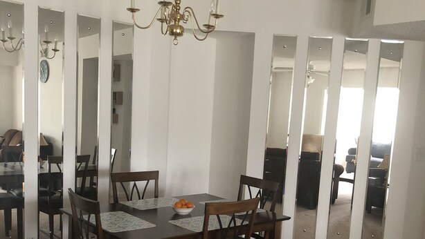 Ein Esszimmer mit Holztisch und -stühlen, einer Kristallleuchtre und drei Spiegeln an der Wand.