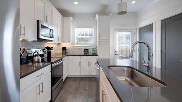 A modern kitchen with white cabinetry, stainless steel appliances, and a large sink.