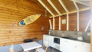 Ein Holzinnenraum mit Küchenbereich, einem Esstisch und Stühlen sowie einem Surfbrett an der Wand.