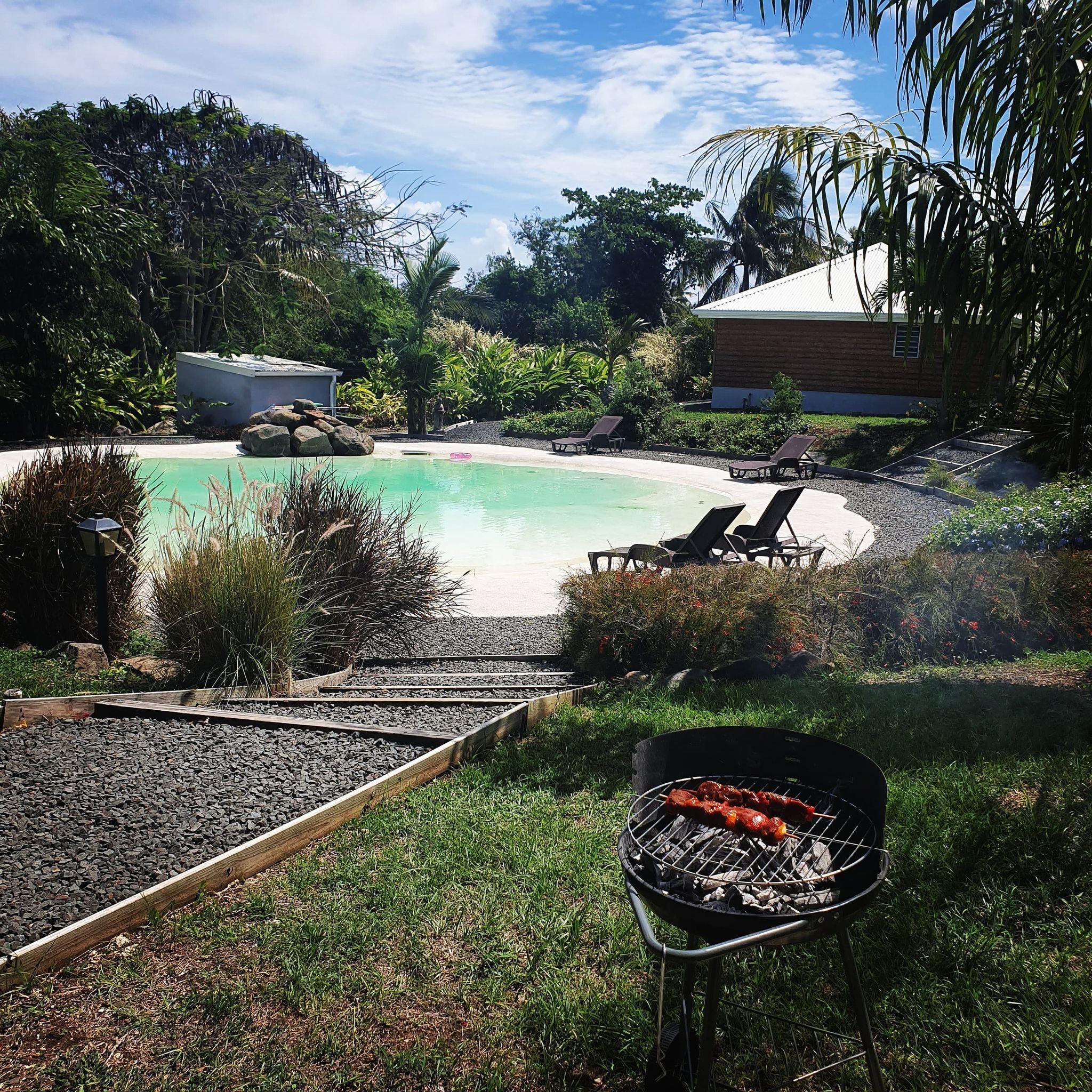 A pool area with lounge chairs, a barbecue grill, and a building in the background.