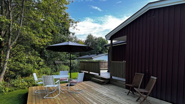 A wooden deck with a table and chairs, an umbrella, and a view of a house and trees. - Wonderful house with new kitchen in beautiful nature and close to activities (Skåne län)