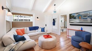Una sala de estar moderna con un sofá blanco, un sillón azul y un otoman redonda.