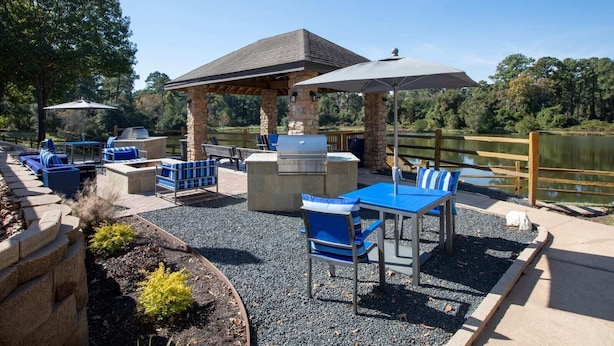An outdoor patio with stone seating, a grill, and a view of a lake. - Total Relaxation and Tranquility - Perfect space for family or work . (The Woodlands)