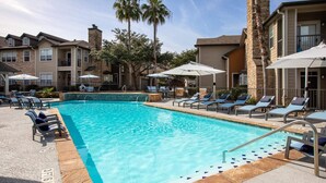 A swimming pool with lounge chairs and umbrellas, surrounded by multi-story buildings with balconies. - Total Relaxation and Tranquility - Perfect space for family or work . (The Woodlands)