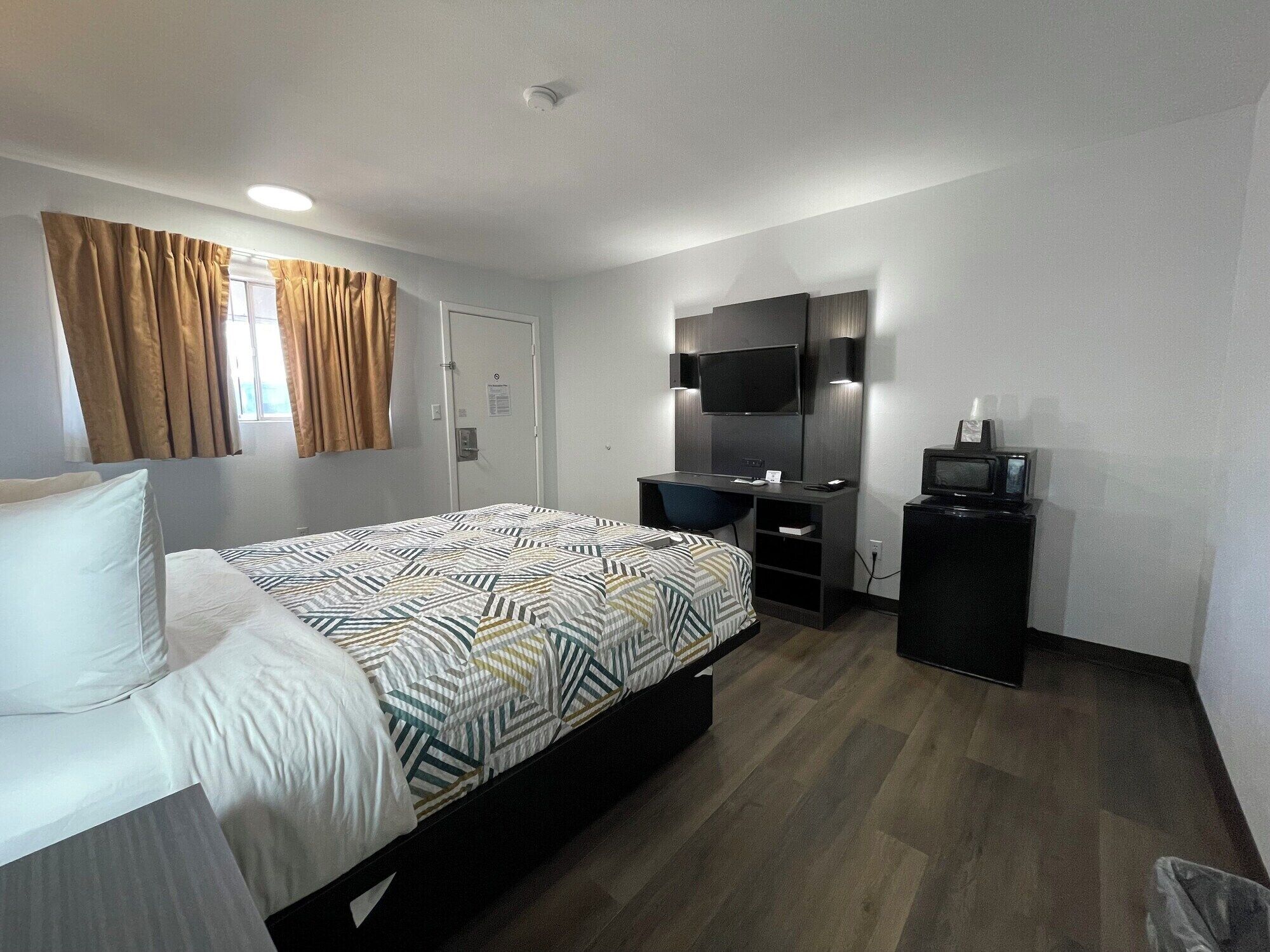 A hotel room with a bed, a desk, a television, and a small cabinet.