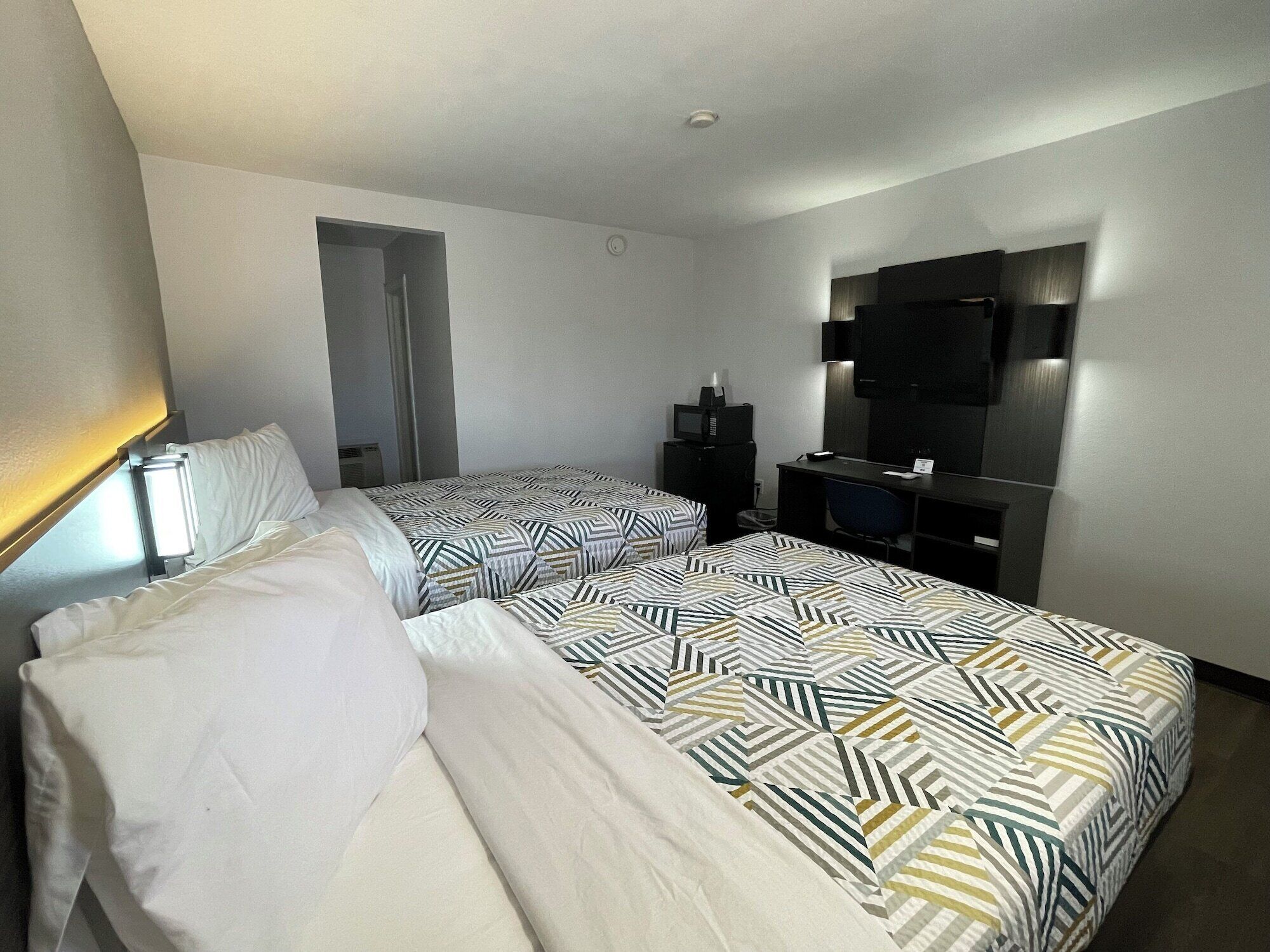 A hotel room with two beds, a desk, a TV, and a mirror.