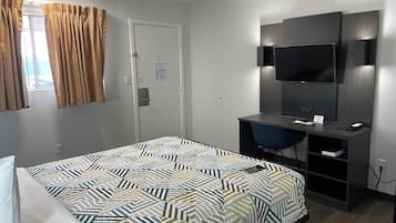 A hotel room with a bed, a desk with a chair, a television mounted on the wall, and a door with a fire evacuation plan.