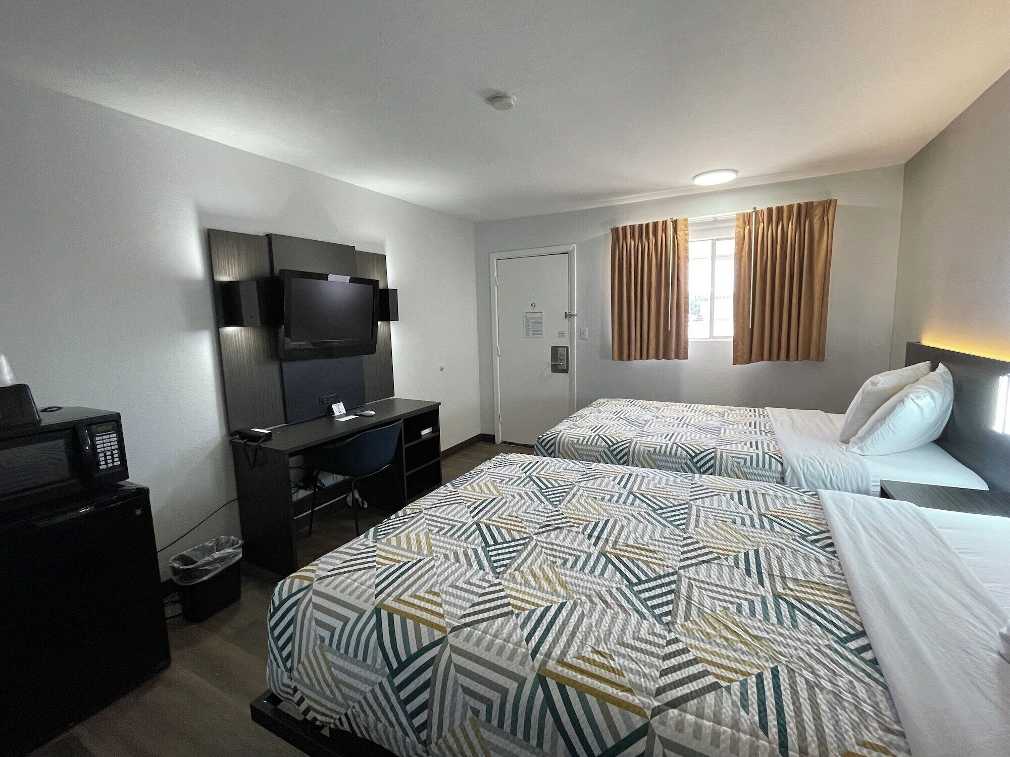 A hotel room with two beds, a desk, a TV, and a microwave.