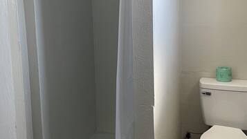 Casa de banho pequena e compacta, com chuveiro, sanita e lavatório.