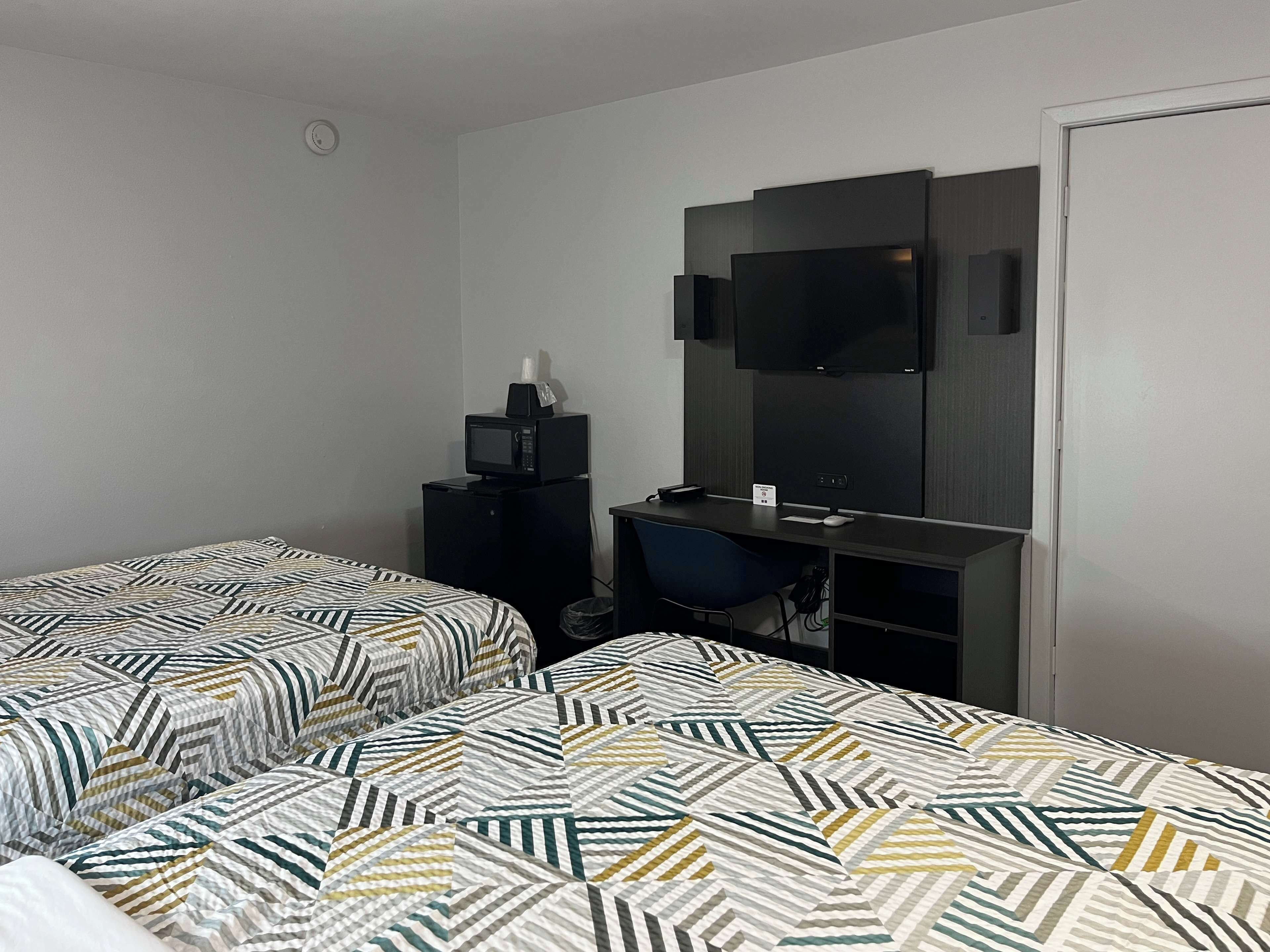 Ein Hotelzimmer mit zwei Betten, Bettwäsche mit Muster, einem Schreibtisch mit Computer, einem Fernseher und einer kleinen Mülltonne.
