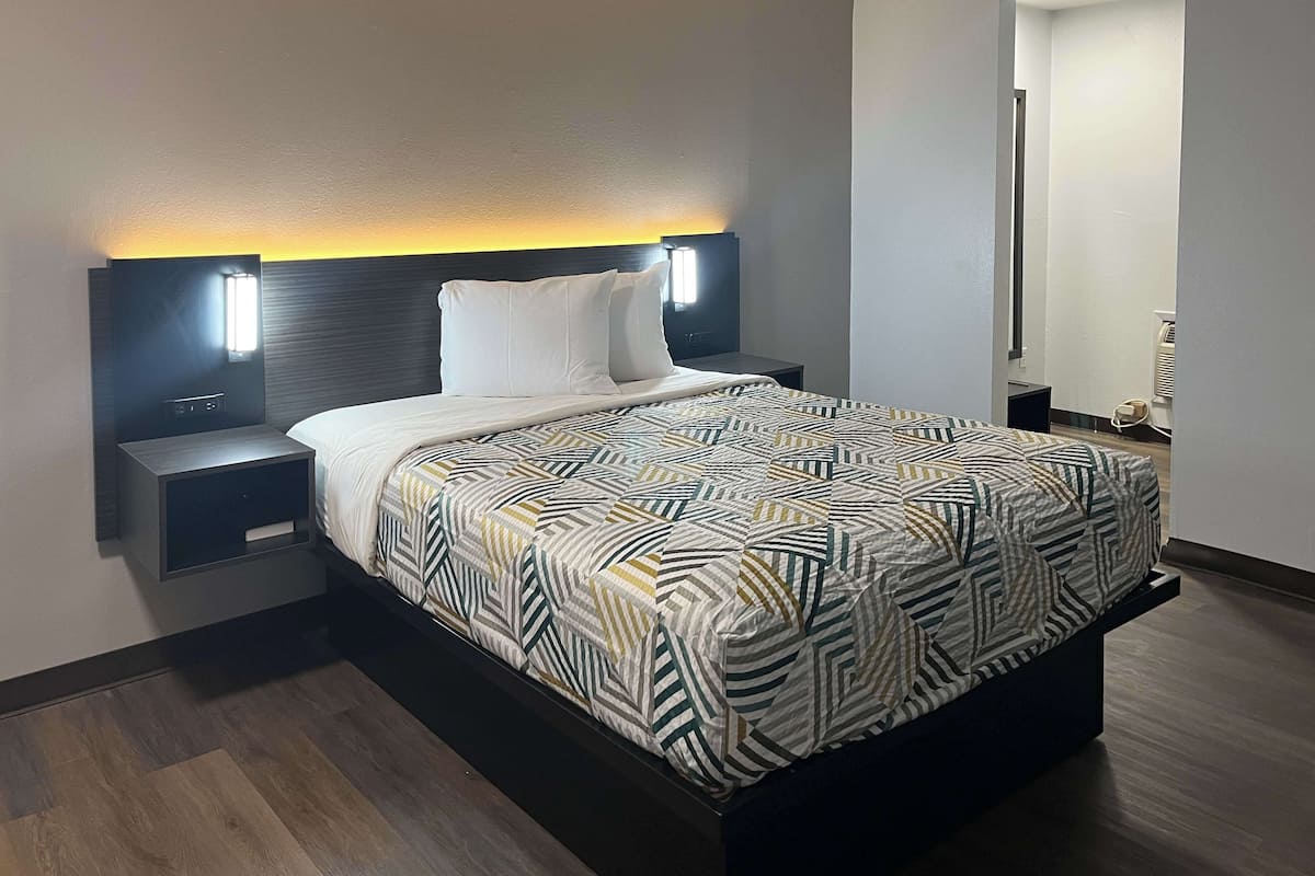 A modern hotel room with a large bed, a nightstand with a lamp, and a mirror on the wall.