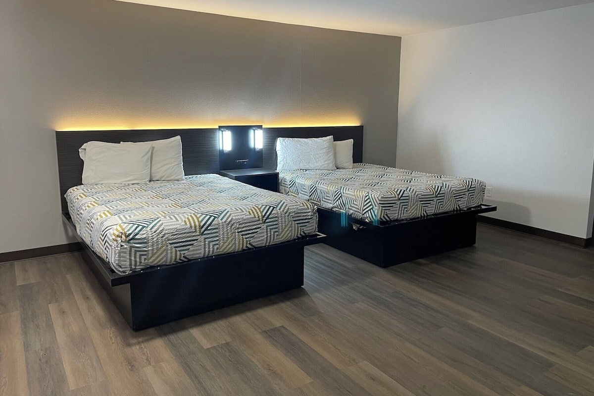 A hotel room with two beds, each with a patterned bedspread and white pillows, against a dark headboard.
