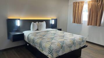 A modern hotel room with a large bed, two bedside tables with lamps, a headboard with built-in lighting, and a window with curtains.