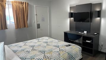 Ett hotellrum med en säng, ett skrivbord, en stol, en tv och en dörr med en skylt som visar utgången i händelse av brand.