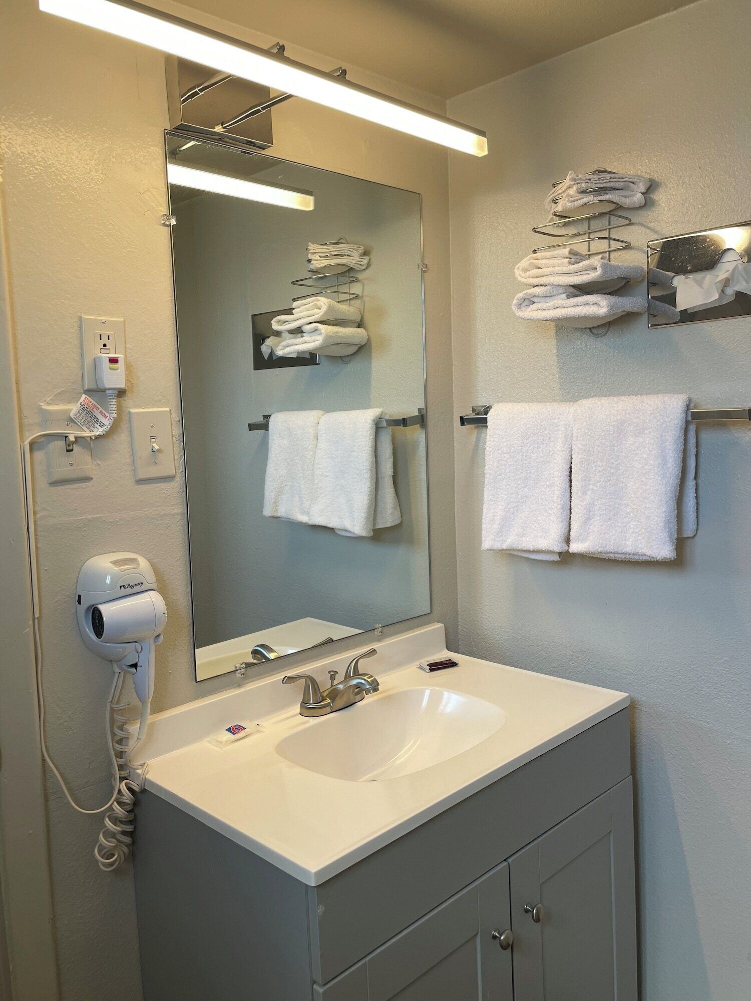 Une salle de bain équipée d’un lavabo, d’un miroir, d’un porte-serviettes et d’un sèche-cheveux.
