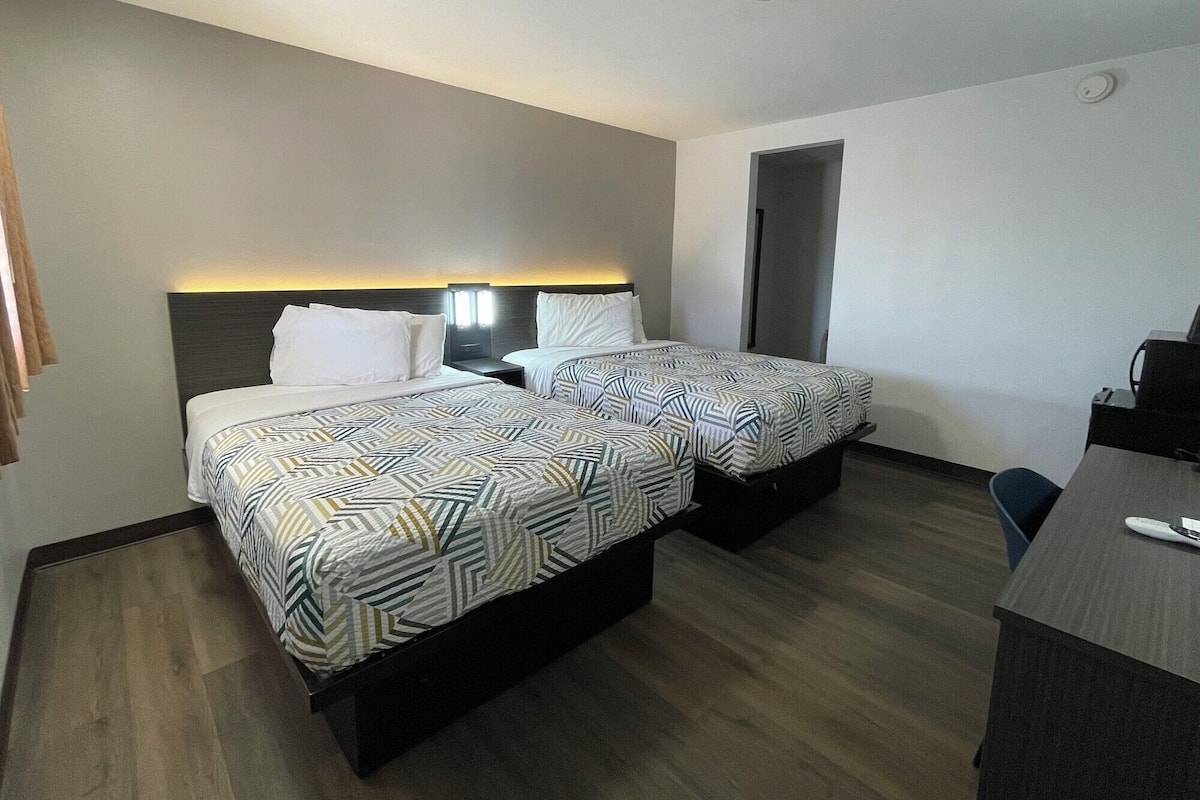 A hotel room with two beds, a desk, and a chair.