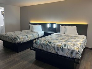 Two beds with geometric patterned bedding, a dark headboard with built-in lighting, and a wooden floor.