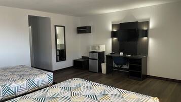 Habitación de hotel con dos camas, un escritorio, una silla, microondas, cubo de basura y televisor.