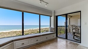 Une pièce dotée d’une grande fenêtre donnant sur une plage, d’une porte-fenêtre coulissante menant à un balcon et d’un banc intégré avec des tiroirs de rangement.