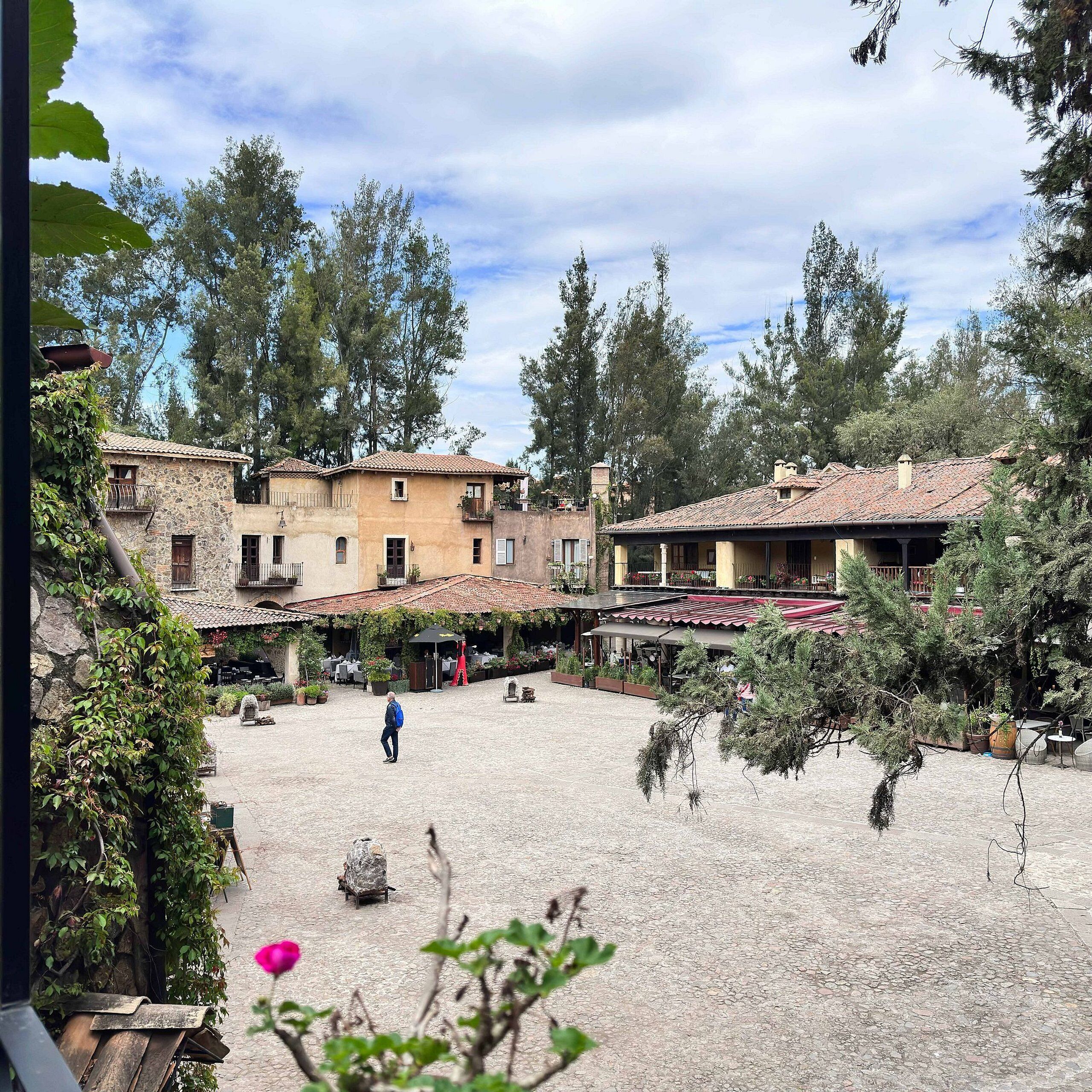A courtyard with stone flooring, surrounded by buildings with tiled roofs and balconies.