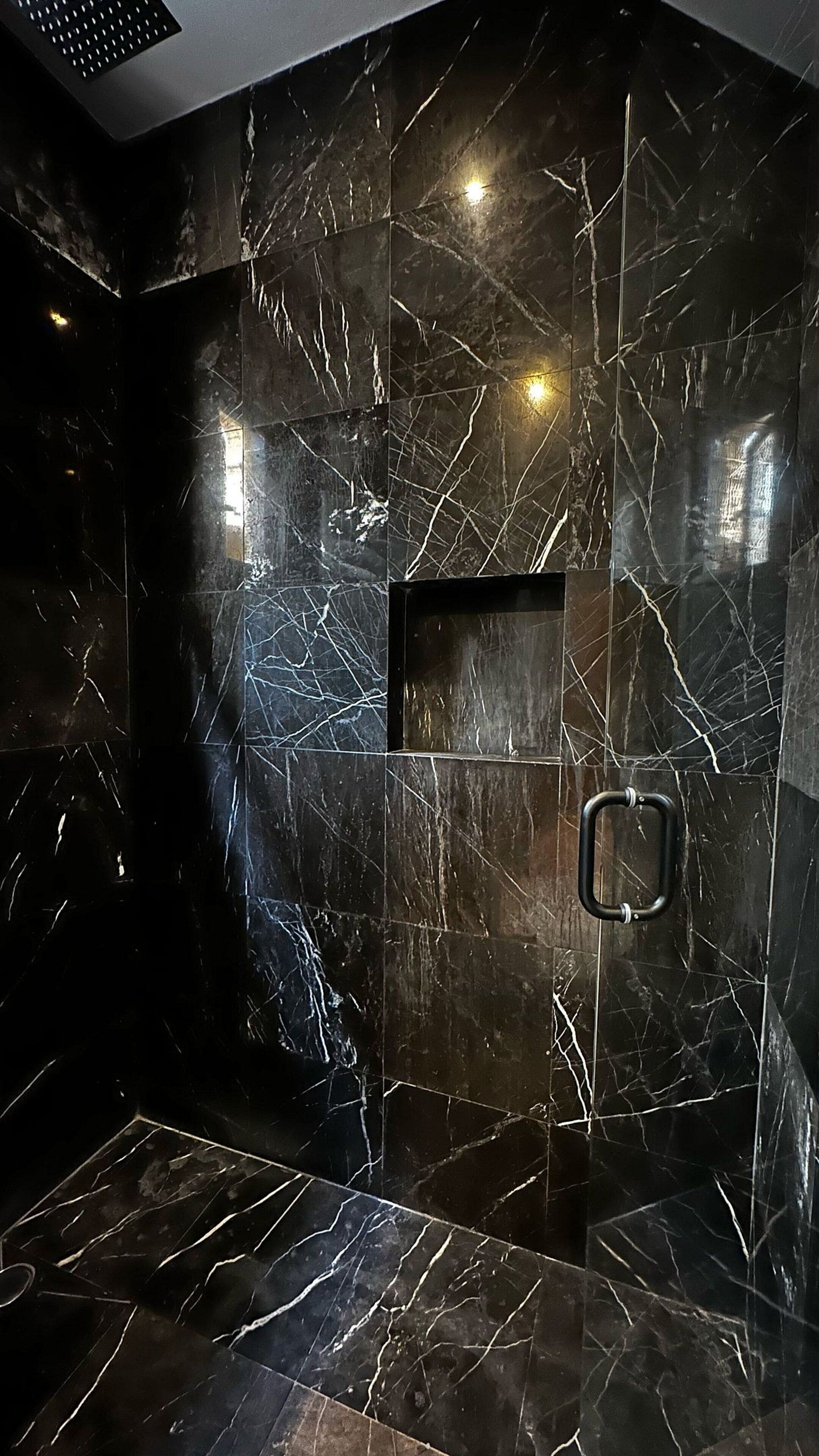 A modern bathroom with black marble walls and floor, a built-in shower, and a towel rack.
