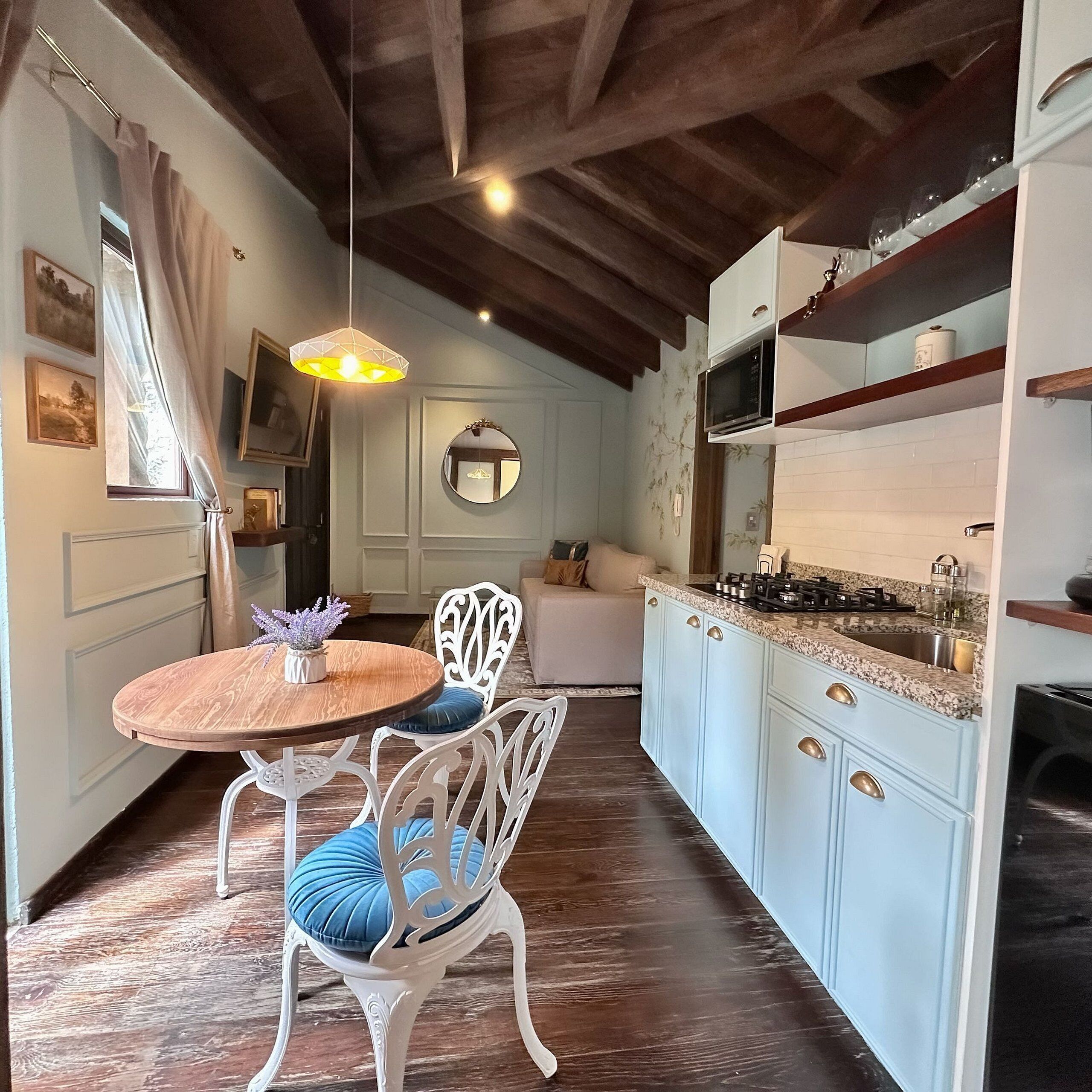 A cozy kitchen with white cabinets, a round wooden table, and a hanging light fixture.