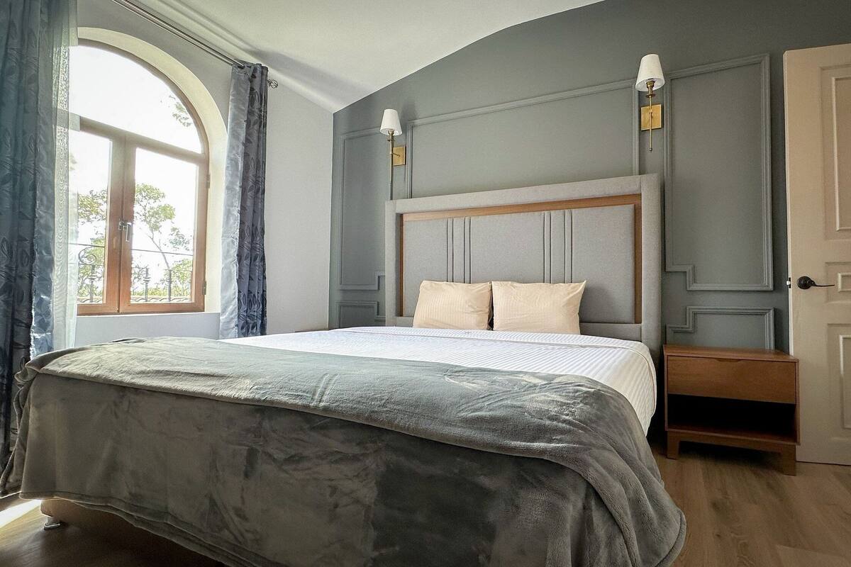 A bedroom with a large bed, a nightstand, a lamp, and a door.
