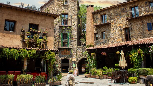 Un patio con edificios de piedra, plantas en macetas y mesas al aire libre.
