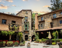 Un patio con edificios de piedra, plantas en macetas y mesas al aire libre.