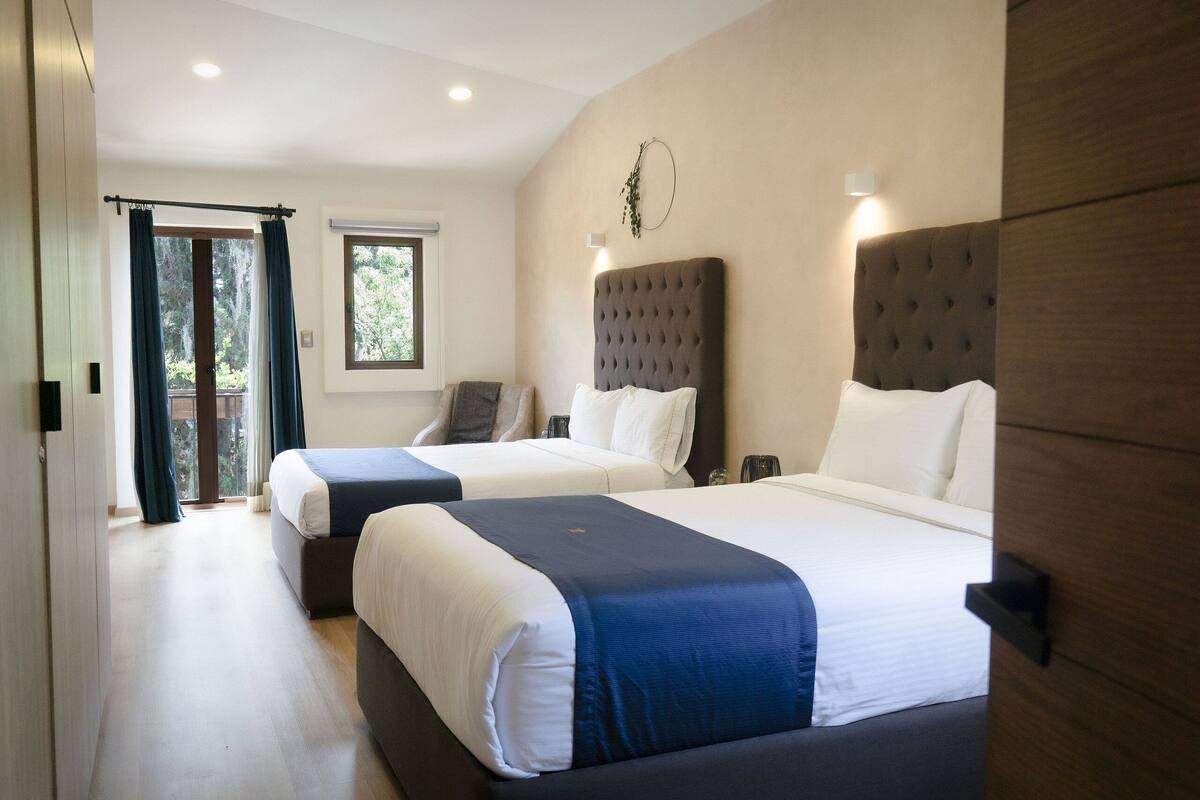 A hotel room with two beds, a large window, and a door leading to a balcony.