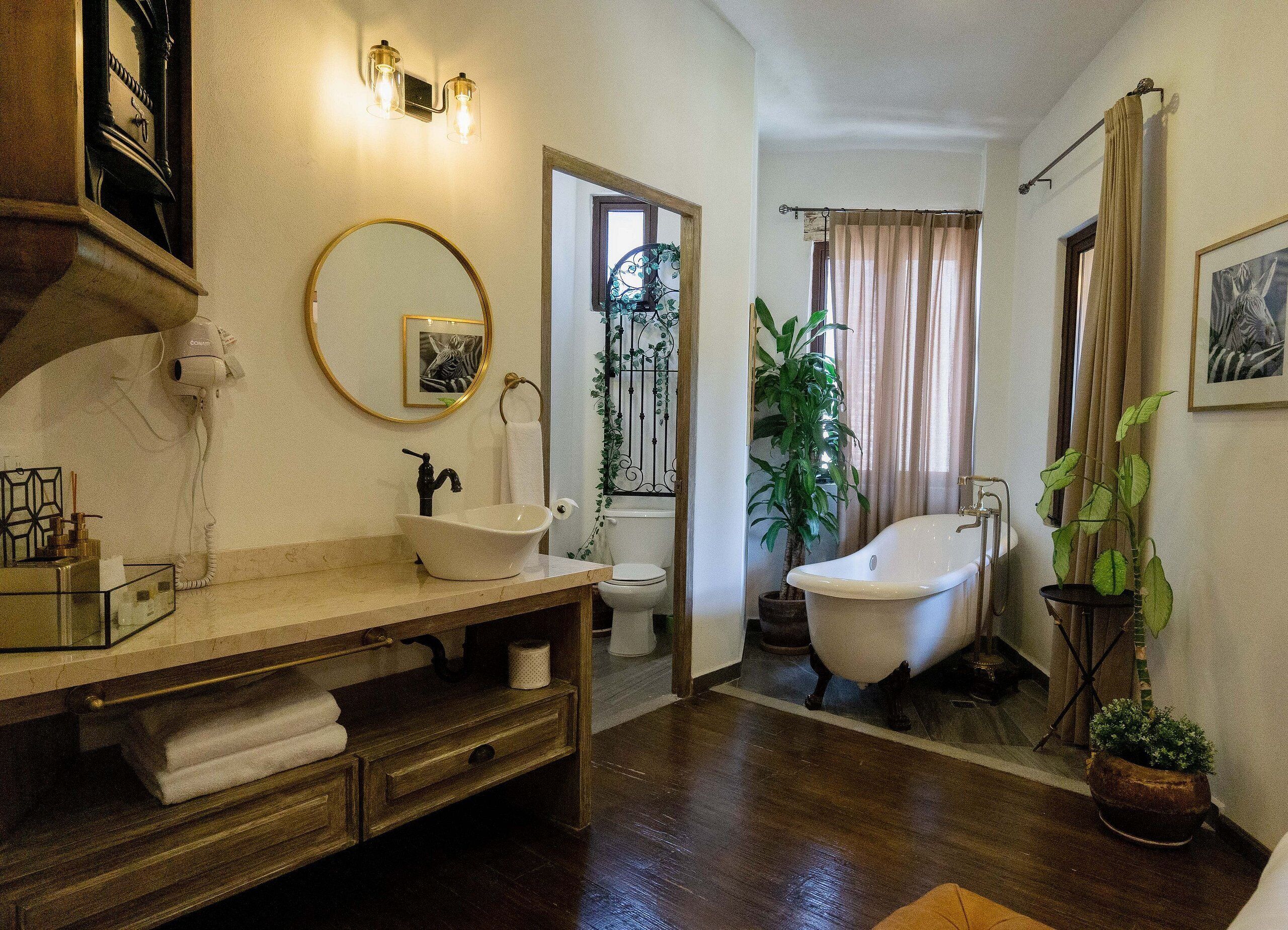 A bathroom with a wooden vanity, a freestanding bathtub, a toilet, and a mirror with a framed picture.