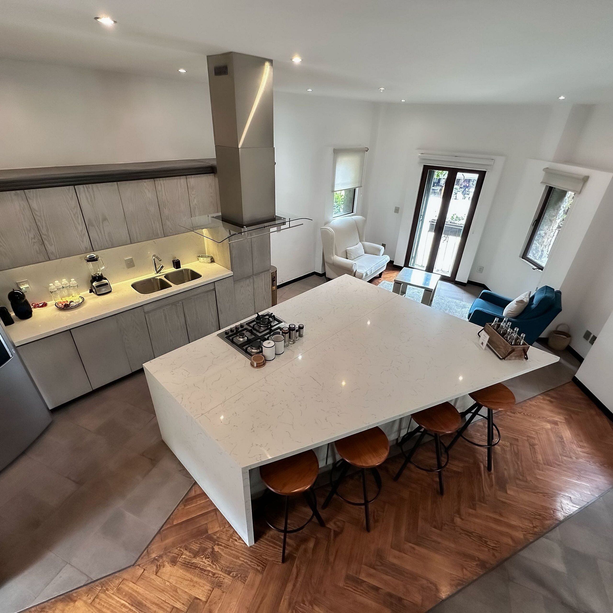 A modern kitchen with a central island, bar stools, and a seating area with a sofa and chairs.