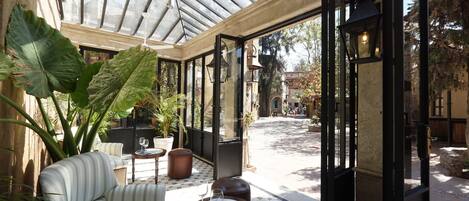 A sunlit patio with a cushioned seating area, a small round table, and a large potted plant.