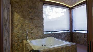 A stone-walled bathroom with a freestanding bathtub, a showerhead, and a window with blinds.