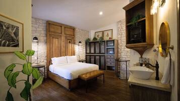Un dormitorio con cama, armario de madera, pared de piedra y baño con lavabo y espejo.