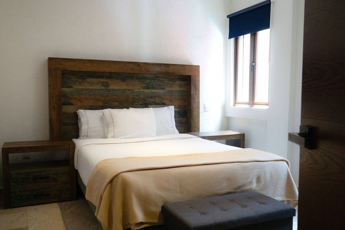 A bedroom with a wooden headboard, a bed with white linens, a bedside table, and a bench.