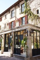 Un edificio con fachada de piedra, ventanas amplias y un balcón con contraventanas rojas.